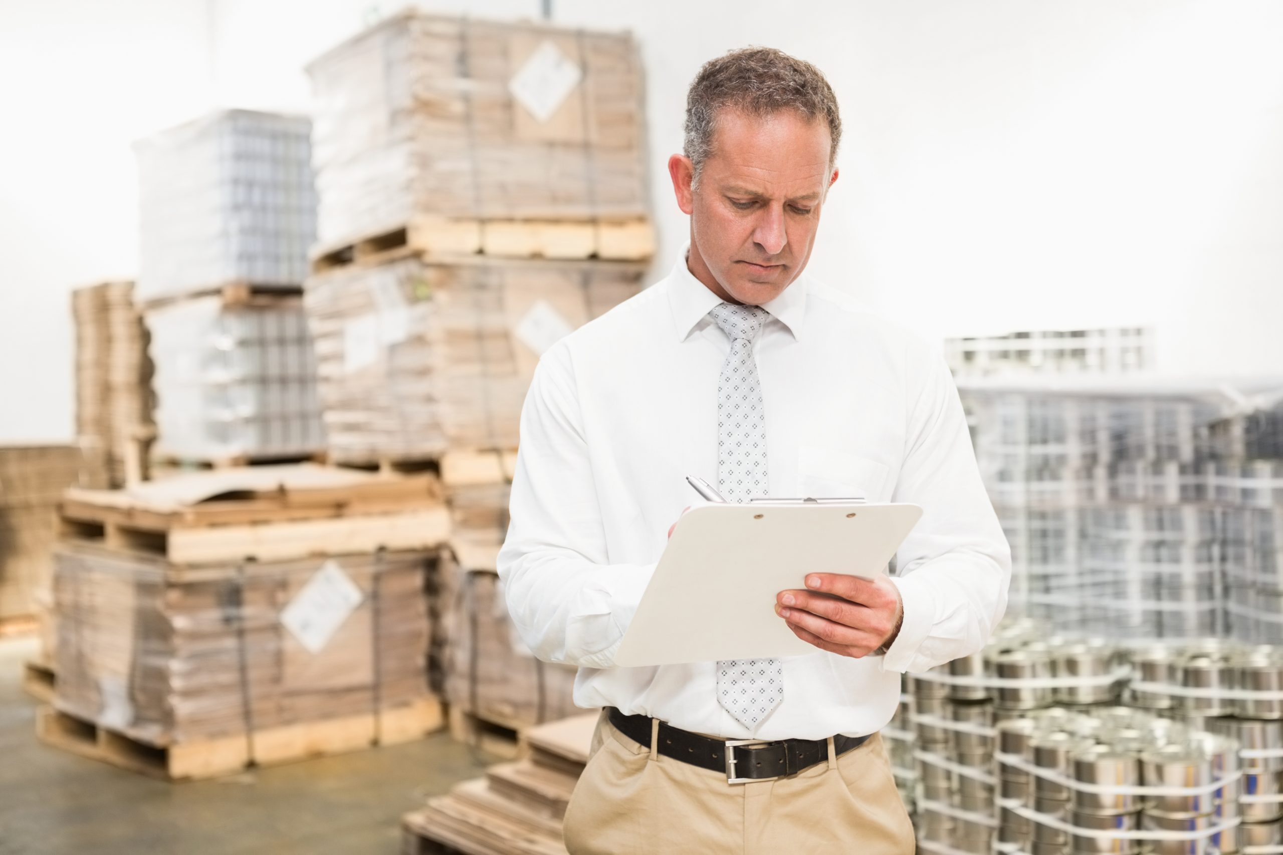 Warehouse manager writing on clipboard in a large warehouse